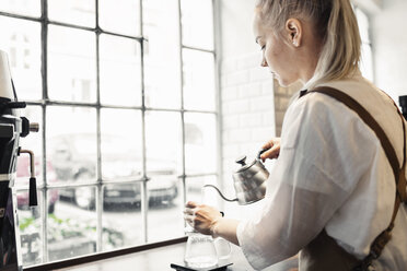 Seitenansicht einer weiblichen Barista, die in einem Café am Fenster Kaffee zubereitet - MASF04793