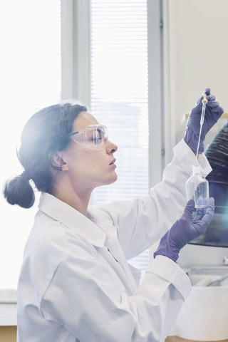 Seitenansicht einer Wissenschaftlerin, die eine Pipette benutzt, während sie eine Chemikalie im Labor untersucht, lizenzfreies Stockfoto