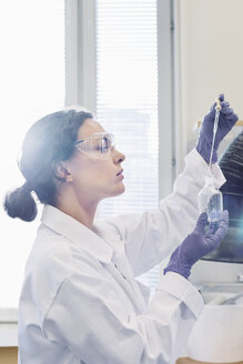 Side view of female scientist using pipette while examining chemical in laboratory - MASF04808