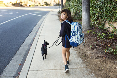 Rear view portrait of girl walking with dog on sidewalk - CAVF41679