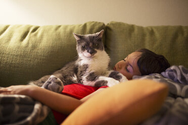 Porträt einer Katze, die auf einem Jungen sitzt, der zu Hause auf dem Sofa schläft - CAVF41697