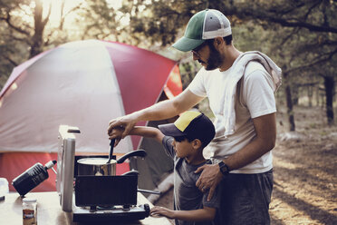 Vater und Sohn bereiten Essen auf einem Campingkocher im Wald zu - CAVF41732