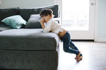 Boy looking away while leaning on sofa at home - CAVF41752