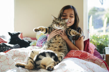 Glückliches Mädchen mit Katze auf dem Bett sitzend zu Hause - CAVF41756