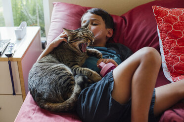 Hochformatige Ansicht eines Jungen mit Katze, der zu Hause auf dem Bett liegt - CAVF41772