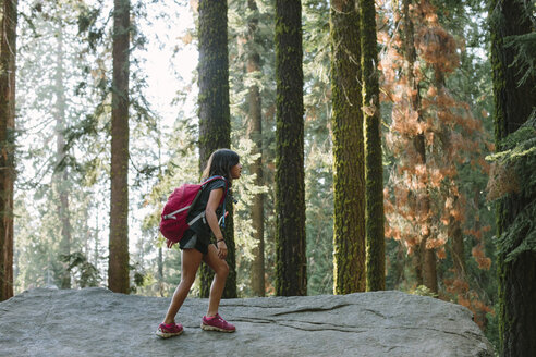 Mädchen mit Rucksack geht auf Felsen im Wald - CAVF41776