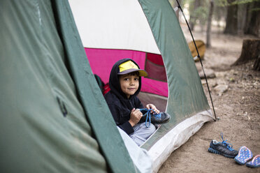 Porträt eines Jungen mit Schuhen, der im Zelt im Wald sitzt - CAVF41780