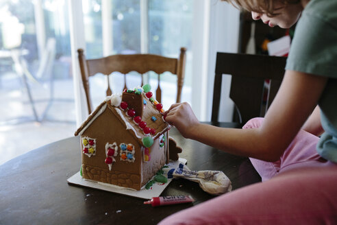 Mädchen dekoriert Lebkuchenhaus auf Tisch zu Hause - CAVF41785