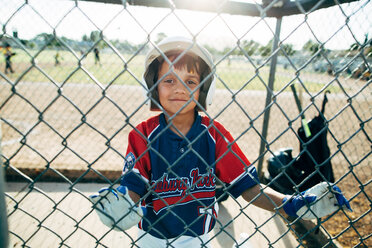 Portrait of happy baseball player standing behind chainlink fence - CAVF41835