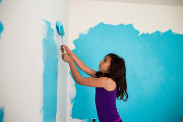 Side view of girl painting wall with paint roller at home - CAVF41843