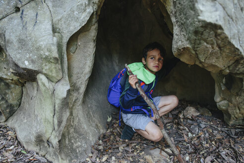 Junge mit Rucksack schaut weg, während er in einer Felsformation hockt - CAVF41859