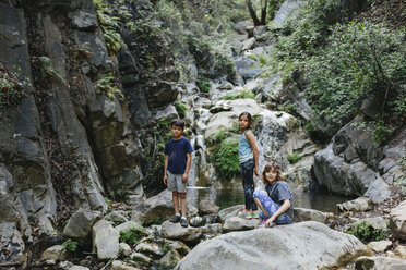 Portrait of sisters on rocks with brother by stream - CAVF41862