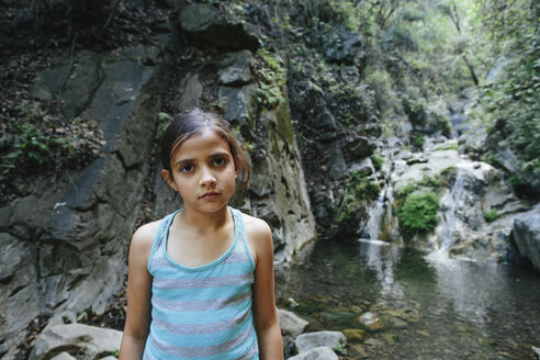 Porträt eines selbstbewussten Mädchens, das vor einem Wasserfall im Wald steht - CAVF41863