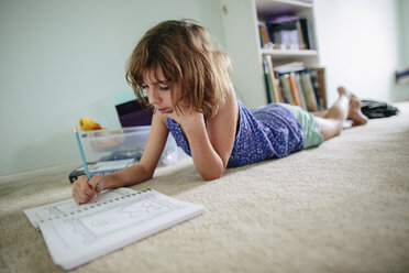 Mädchen macht Hausaufgaben, während sie zu Hause auf dem Boden liegt - CAVF41872
