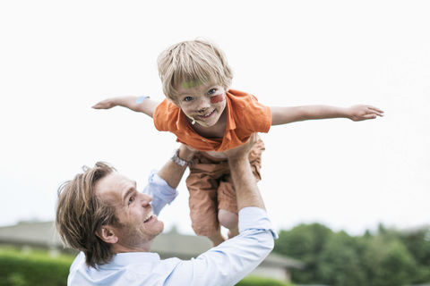 Verspielter Vater hebt verletzten Sohn gegen den klaren Himmel, lizenzfreies Stockfoto