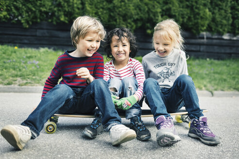 Verspielte Freunde sitzen auf dem Skateboard im Hof - MASF04847