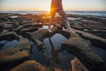 Low section of woman walking at rocky beach during sunset - CAVF41893