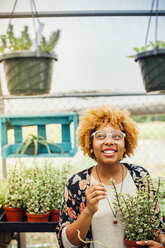 Glückliche Frau schaut weg, während sie eine Topfpflanze in einer Gärtnerei hält - CAVF41921