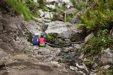 Rear view of siblings crouching on rocks and looking at flowing water - CAVF41964