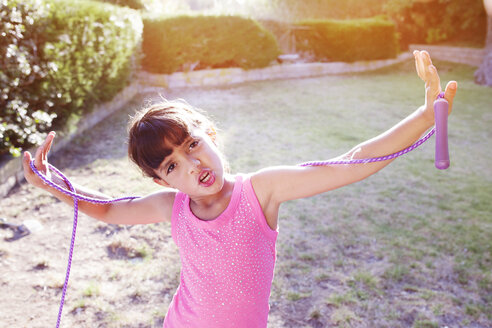 Porträt eines Mädchens, das ein Springseil mit ausgestreckten Armen auf einem Feld hält - CAVF41998