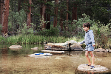 Glücklicher Junge steht auf einem Felsen am Bach vor Bäumen - CAVF42008