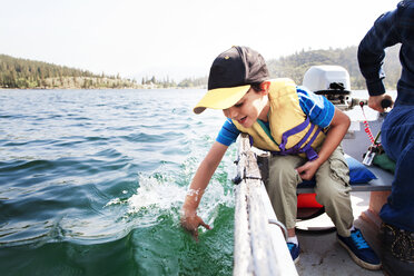 Glücklicher Sohn spielt im Wasser, während er mit seinem Vater in einem Motorboot auf dem See unterwegs ist - CAVF42018