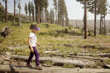 Seitenansicht eines Mädchens, das auf einem Feld auf Holz läuft - CAVF42027