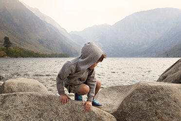 Junge hockt auf Felsen vor dem Convict Lake und den Bergen - CAVF42048