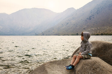 Junge sitzt auf einem Felsen am Convict Lake und blickt auf die Berge - CAVF42049