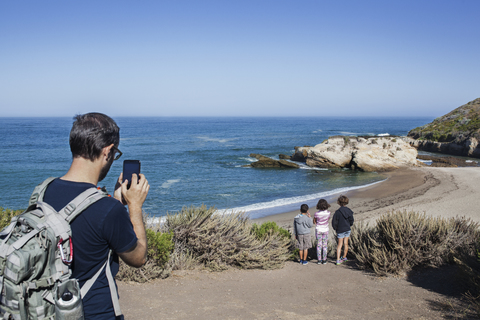 Vater fotografiert Kinder am Strand gegen den Himmel, lizenzfreies Stockfoto