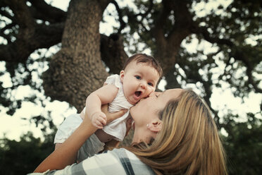 Nahaufnahme von Mutter küsst Baby Tochter gegen Bäume - CAVF42078
