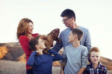 Glückliche Familie mit Hund auf einem Feld vor klarem Himmel - CAVF42087