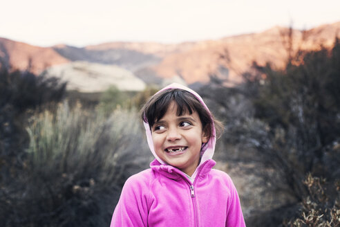 Happy girl wearing pink hood while standing on field - CAVF42107