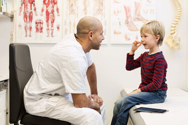 Male orthopedic doctor talking to boy sitting on examination table in clinic - MASF04863