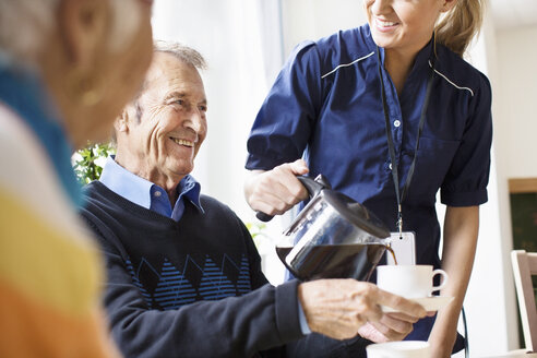 Mittelteil eines glücklichen weiblichen Pflegers, der einem älteren Mann im Pflegeheim schwarzen Kaffee serviert - MASF04902