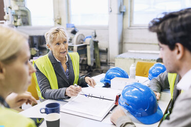 Ältere Arbeitnehmerin im Gespräch mit Kollegen am Tisch in einer Fabrik - MASF04913