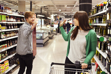 Mann und Frau winken sich im Supermarkt zu - MASF04915