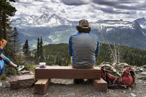 Rückansicht eines auf Holz sitzenden Mannes vor einem Berg, lizenzfreies Stockfoto