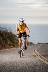 Man cycling on road against sea - CAVF42161