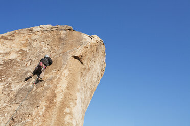 Low angle view of man rock climbing against clear blue sky - CAVF42167
