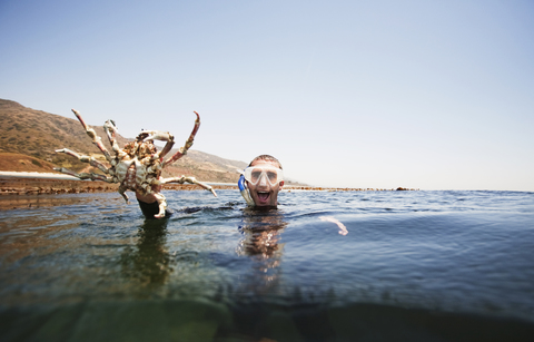 Porträt eines aufgeregten Mannes, der beim Schwimmen im Meer eine große Krabbe hält, lizenzfreies Stockfoto