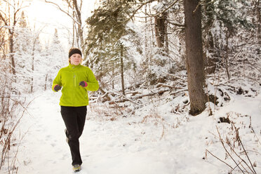 Woman running by trees on snow covered field in forest - CAVF42202