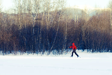 Frau in voller Länge beim Skifahren auf schneebedecktem Feld neben kahlen Bäumen - CAVF42217