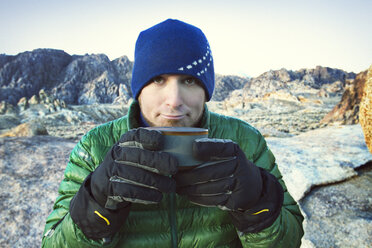 Porträt eines Mannes, der eine Kaffeetasse hält und im Winter auf einem Felsen sitzt - CAVF42250