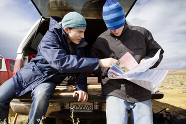 Freunde lesen eine Karte, während sie sich auf einem Feld an den Kofferraum eines Autos lehnen - CAVF42263