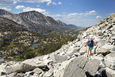 Hiker walking on rocks by mountains against sky - CAVF42308