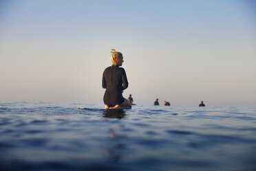 Rückansicht einer Frau, die auf einem Surfbrett auf dem Meer vor einem klaren Himmel ruht - CAVF42309