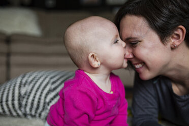 Playful daughter biting mother's nose on bed at home - CAVF42328