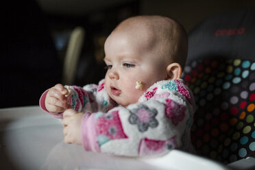 Baby-Mädchen isst Frühstücksflocken, während sie auf dem Hochstuhl zu Hause sitzt - CAVF42330