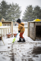 Seitenansicht eines Jungen beim Schneeräumen mit einer Schaufel im Hof - CAVF42334